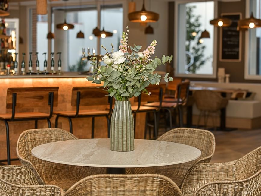 Table avec vase de fleurs et chaises en osier dans un bar à Hôtel Rivella.