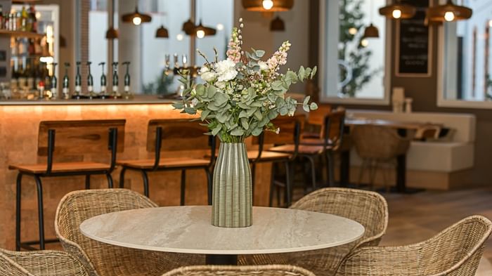 Table avec vase de fleurs et chaises en osier dans un bar à Hôtel Rivella.