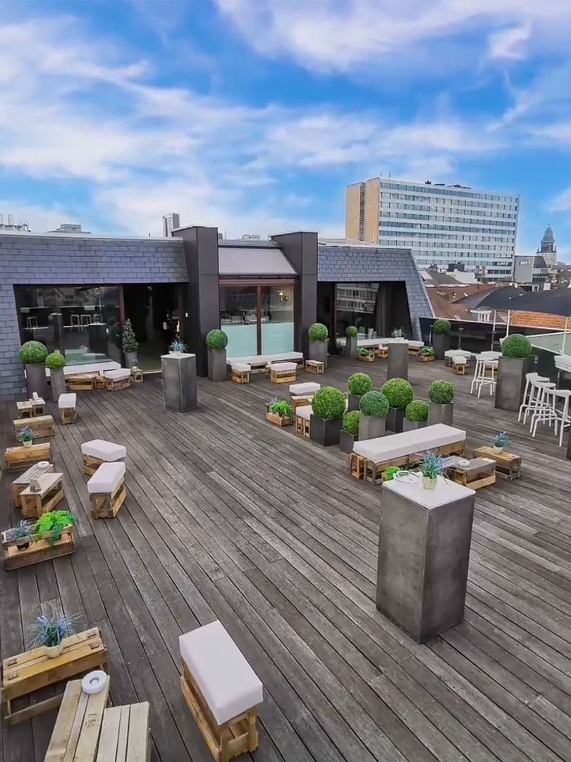 Secret-rooftop with small tables and benches placed by potted plants at Warwick Grand Place Brussels