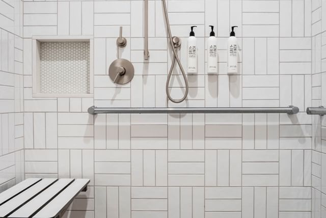 A clean and modern shower with a bench, grab bar, and soap dispensers.