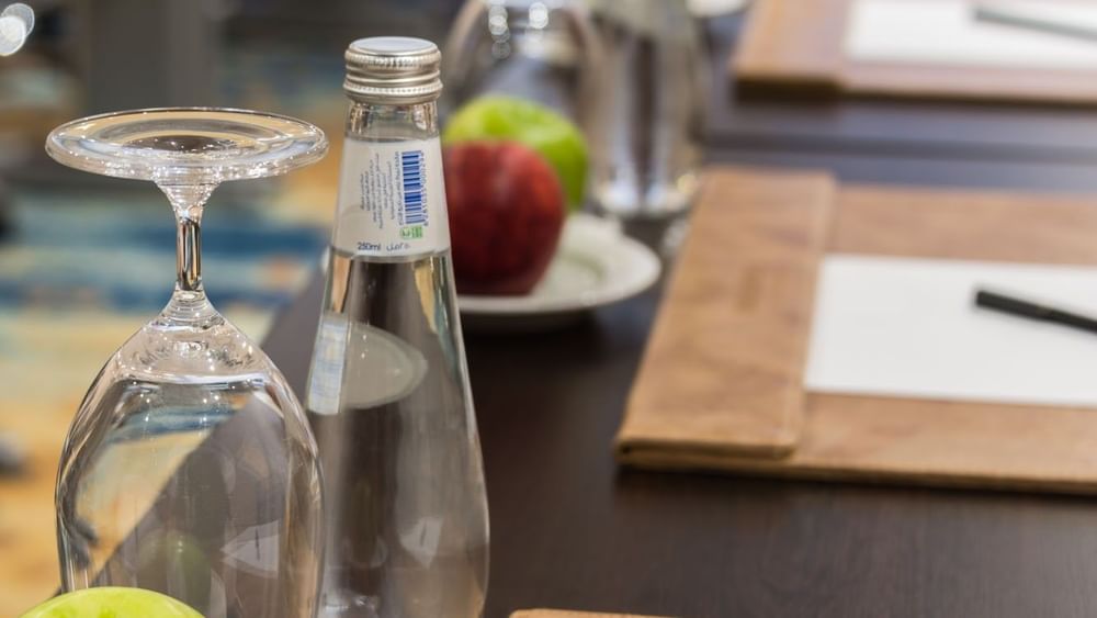 Close-up table featuring a glass by water near apples & an inverted glass in Khalej Meeting Room at Naviti by Warwick Dammam