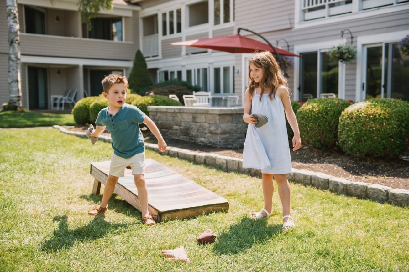 Two children playing on a lawn in front of a building.