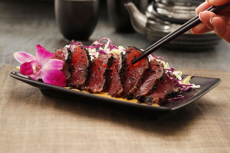 Dish of sliced, sesame-crusted ahi tuna with slaw and a pink orchid served in Chandler's Steakhouse at Hotel 43 Boise