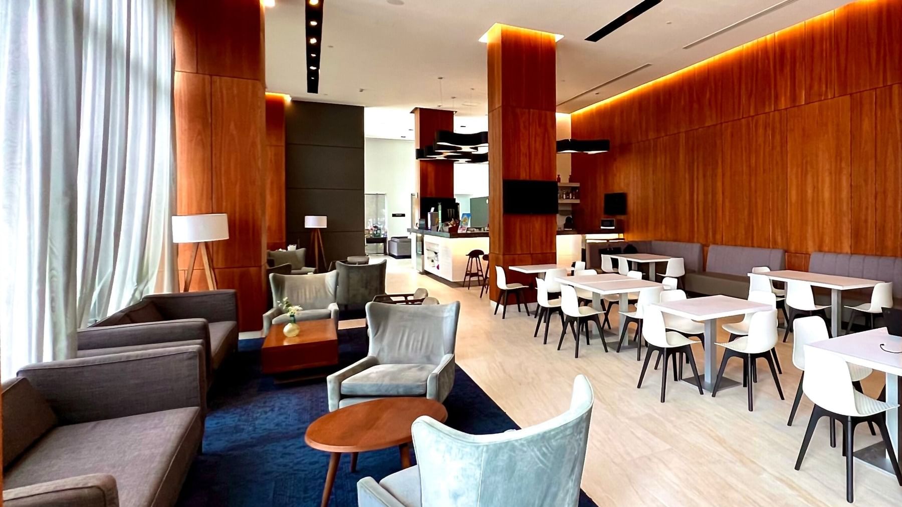 Lobby seating area with sofas & chairs on a blue rug, by tables at Fiesta Inn Express Cancun Cumbres