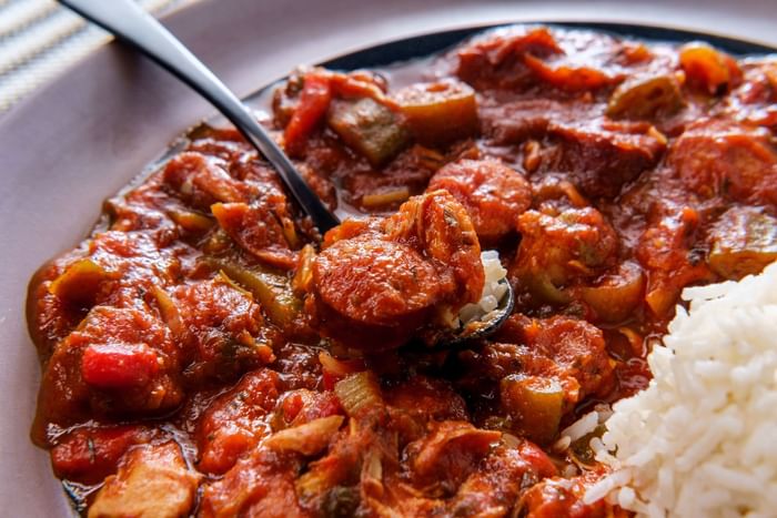 Spicy sausage stew by white rice in a shallow bowl featuring Camo Eats at Anaheim Portofino Inn & Suites