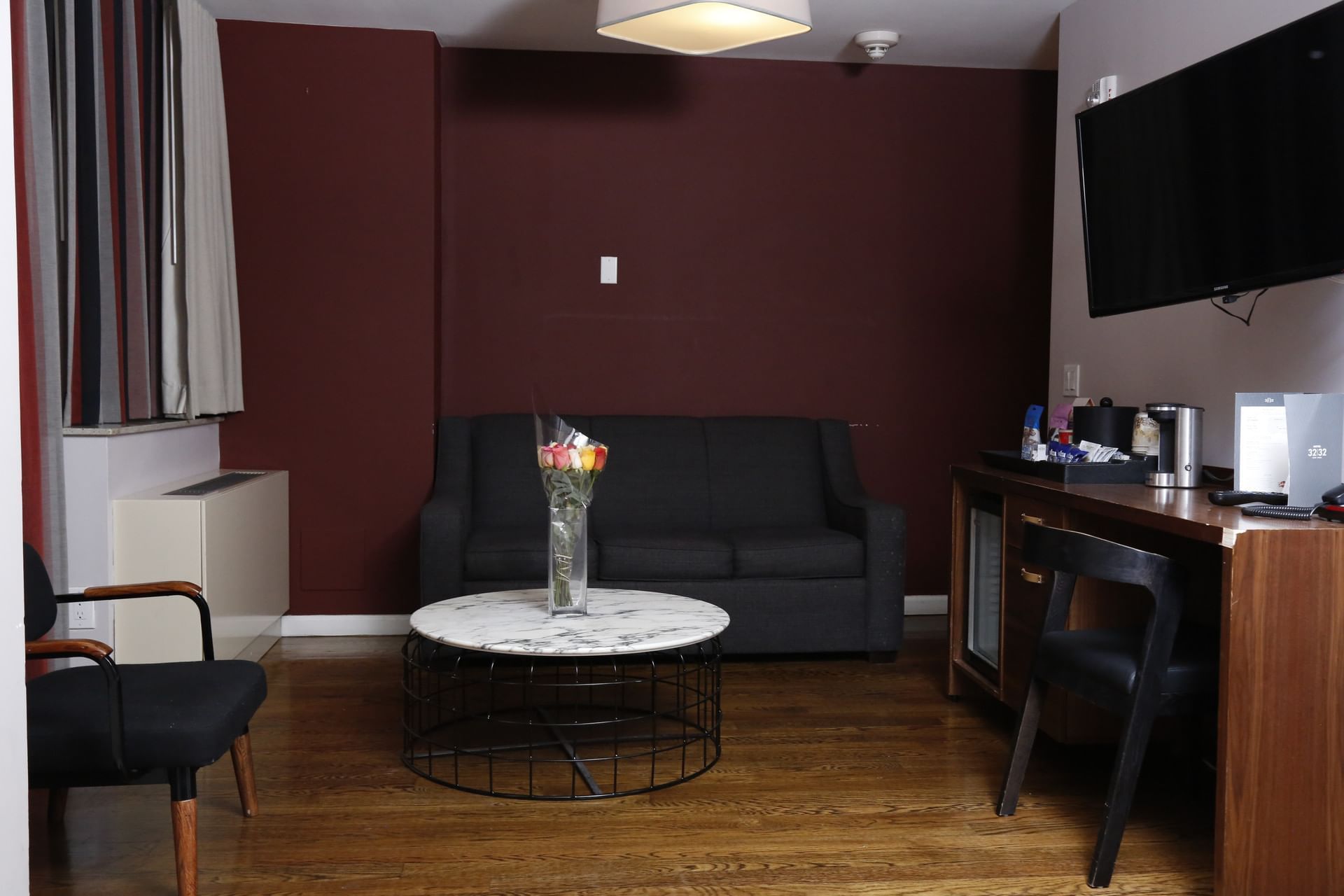 A hotel suite with a sofa, desk, TV, and marble coffee table with flowers.