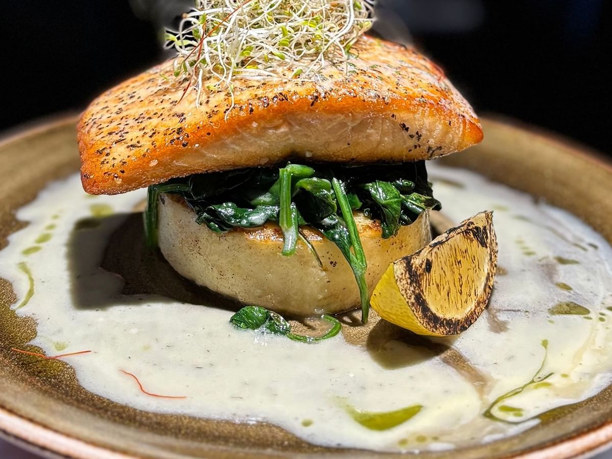 Plate with salmon, spinach, creamy sauce, and garnished with sprouts and lemon wedge.