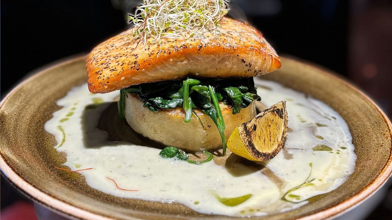 Plate with salmon, spinach, creamy sauce, and garnished with sprouts and lemon wedge.