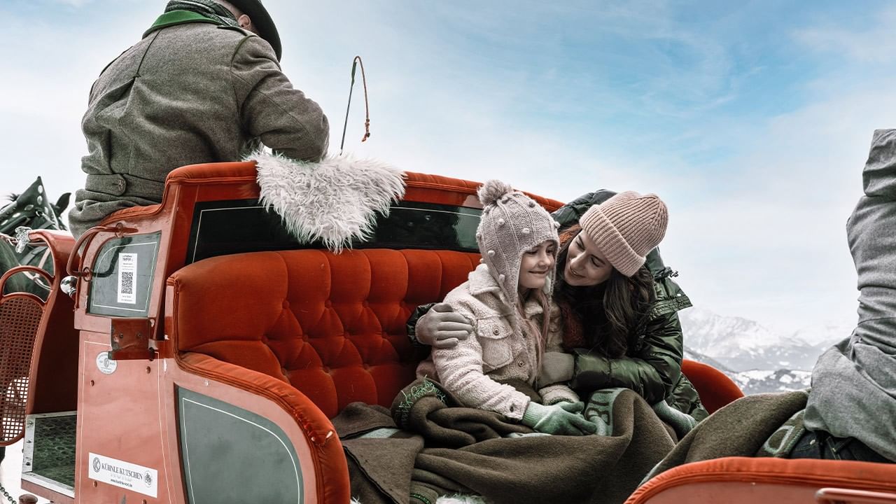 Mutter und Tochter in einer orangefarbenen Kutsche sitzend, während ein Mann auf dem Sitz steht.