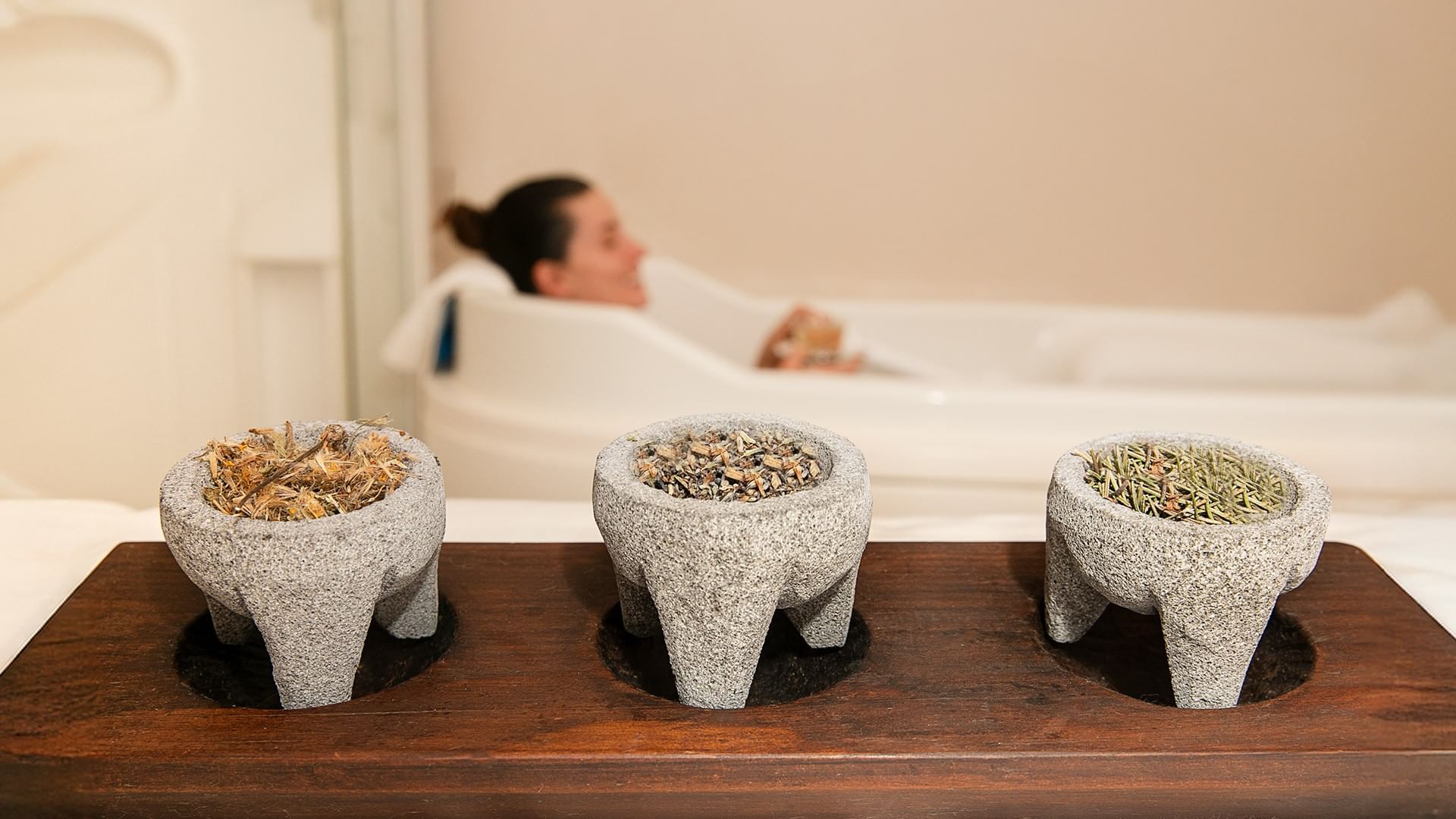 Three mortars with herbs sit on a wooden tray in front of a person in a bathtub at the Marquis Reforma Hotel spa.