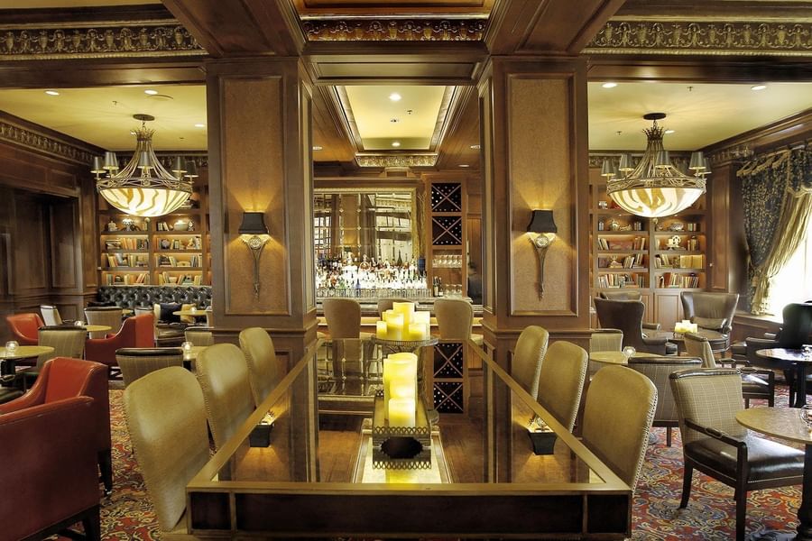 Elegant dining area with modern chandeliers, bookshelves, leather chairs, and a candlelit glass table at The Library Bar