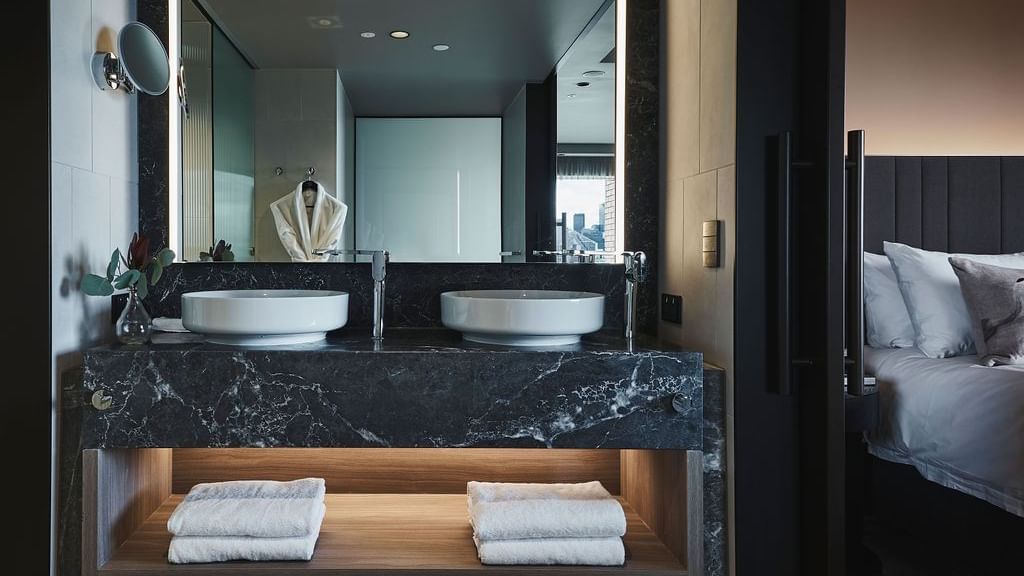 Superior Suite bathroom with dual vessel sinks on black marble vanity and white towels at Pullman East Melbourne.