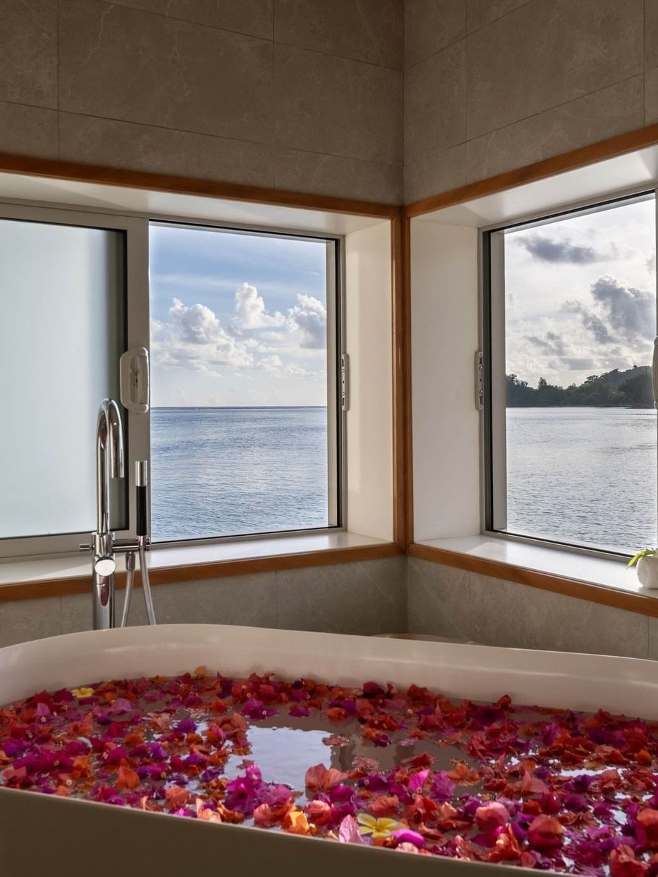 Bathtub filled with pink flower petals facing windows with scenic ocean view in Overwater Villa at warwick le lagon-vanuatu 