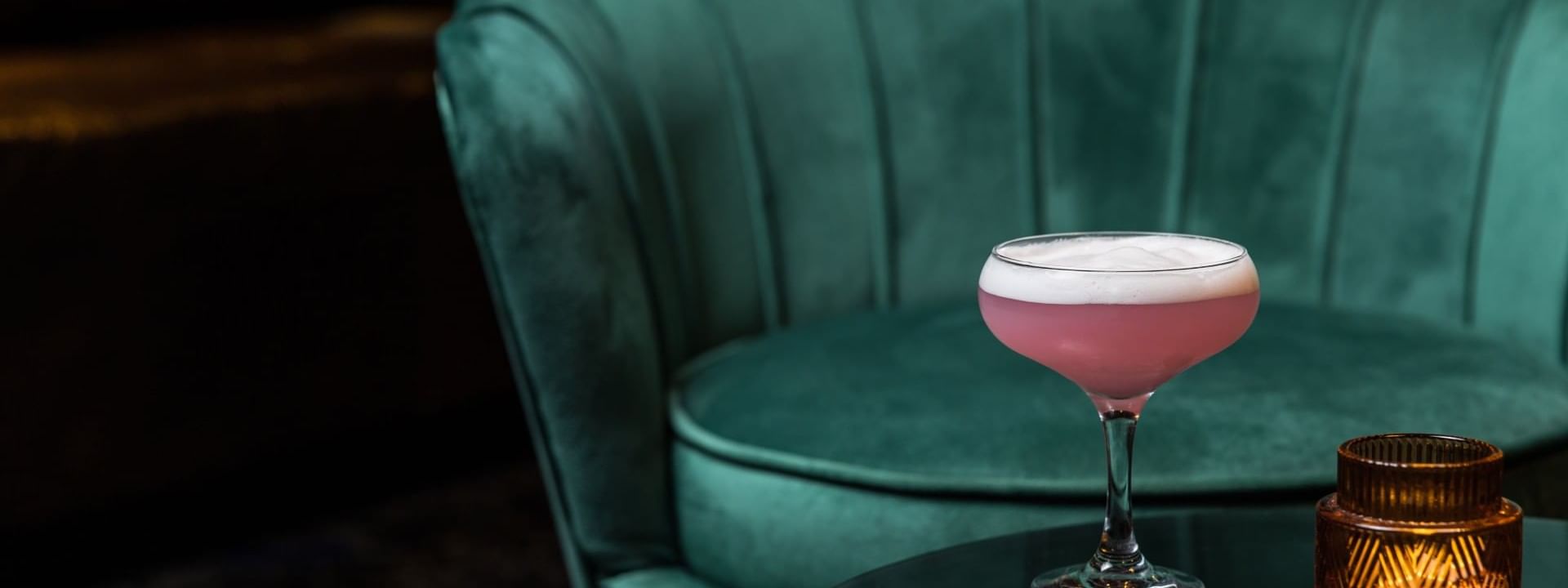 Cocktail on stem glass beside a velvet chair in Minq Bar Lounge at Crown Hotels Perth
