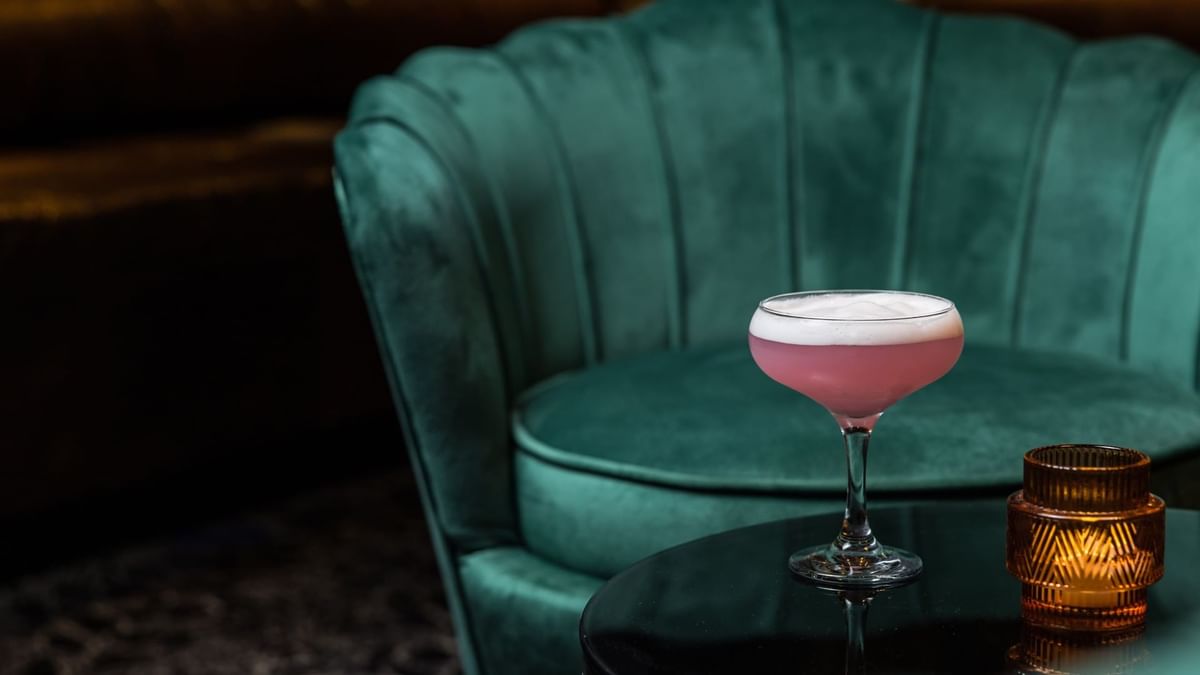 Cocktail on stem glass beside a velvet chair in Minq Bar Lounge at Crown Hotels Perth