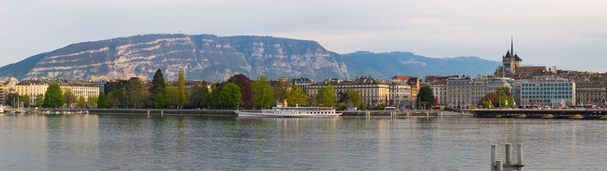 Panoramic city view featuring a white boat by a tree-lined shore near Warwick Geneva