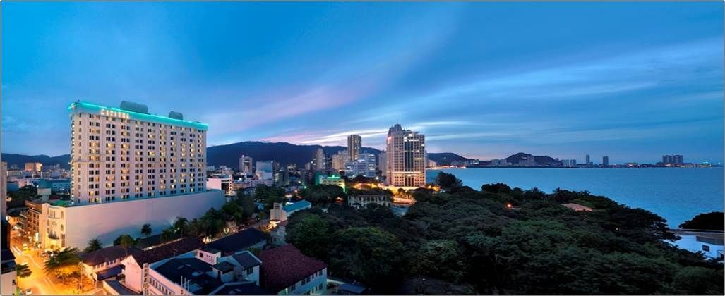 Panoramic dusk view of Cititel Penang Hotel and coastline, city lights twinkling under a vibrant blue sky