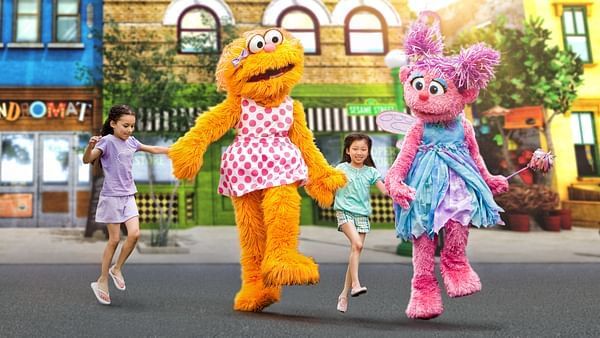 Sesame Street characters skip and hold hands with two young girls in the street. Sesame Street Land at SeaWorld Orlando is a Certified Autism Center, making it a great place to celebrate the holidays with a loved one with special needs.