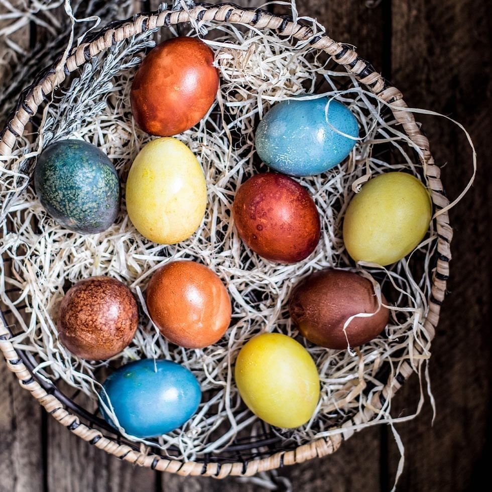 Varie uova colorate in un cestino di vimini su una tavola di legno.