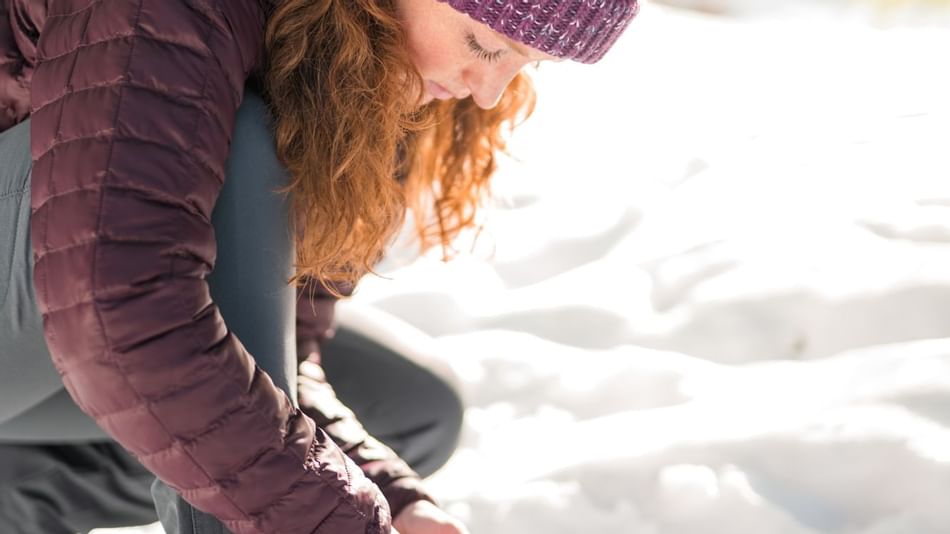 A girl adjusting her snowshoe near The Lake House