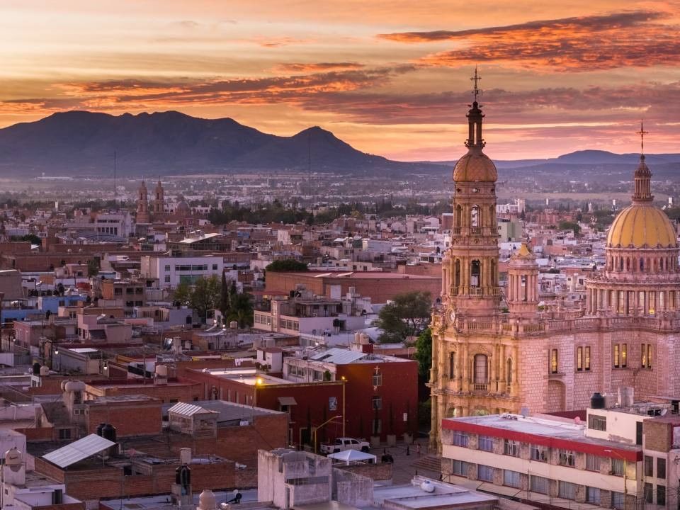 Golden sunset over a historic city skyline with mountains in the distance near Quinta Real Aguascalientes