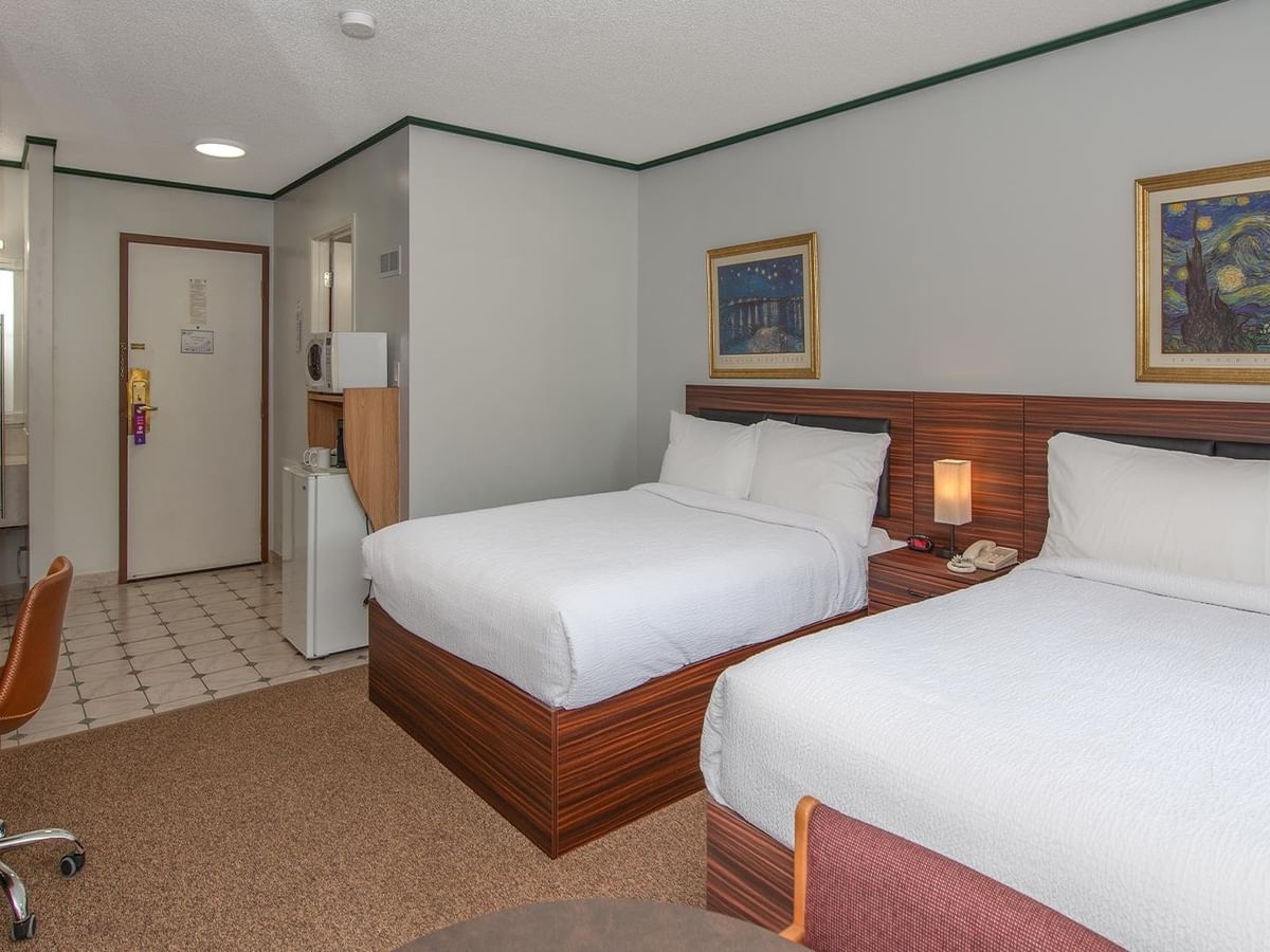 Guest room with two queen beds, bedside lighting and wall art