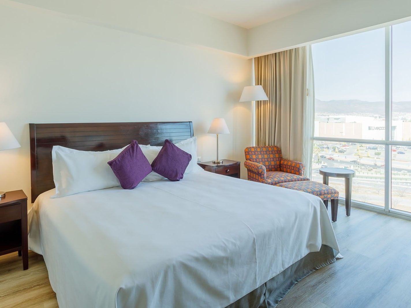 King Deluxe room with a large bed, purple accents, and a desk overlooking the urban landscape at Camino Real Pachuca