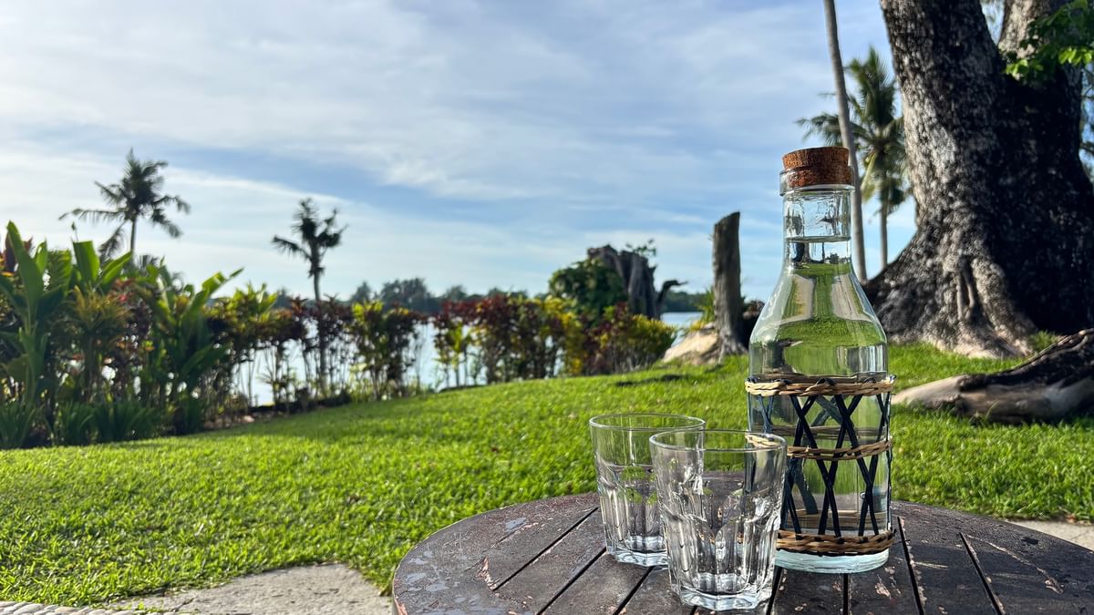 Bottle and two glasses on wooden table with lagoon view at Warwick Le Lagon - Vanuatu, Efate.