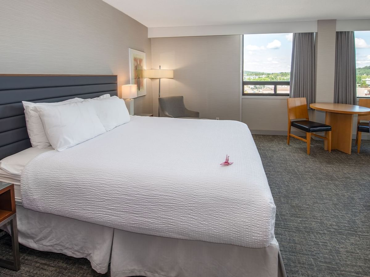 A hotel suite with a king bed, chairs, a round table, and windows.