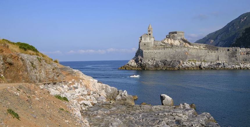 Chiesa di San Pietro su isolotto roccioso nel mare blu con barca in lontananza.