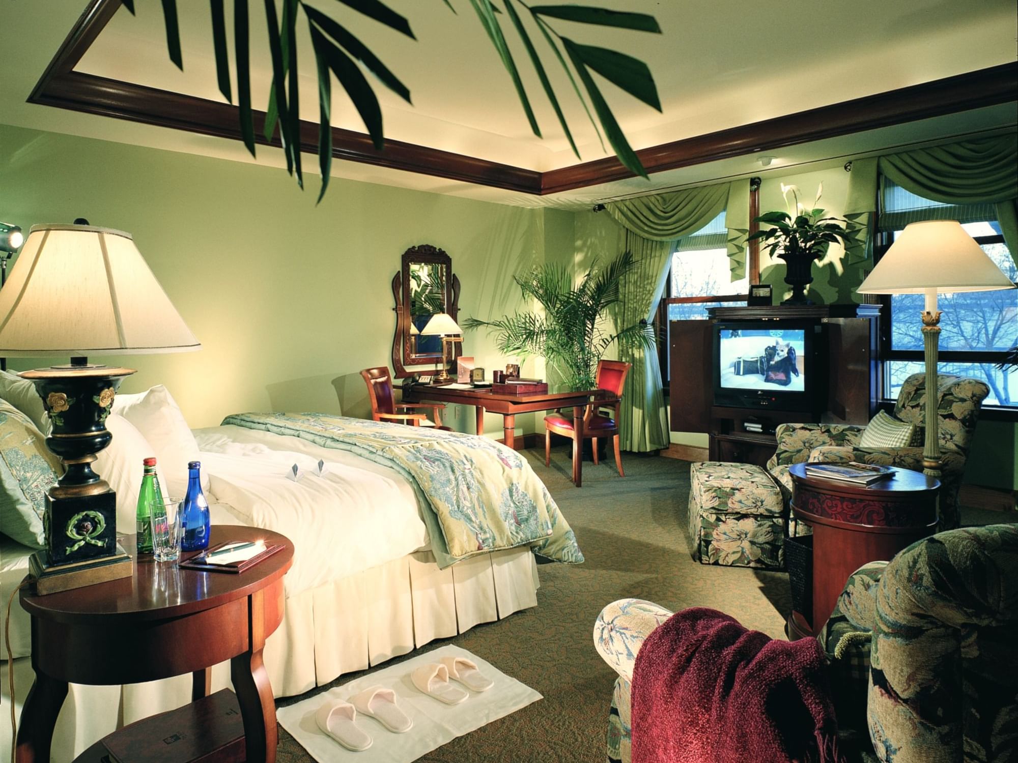 Deluxe King featuring a bed, desk, seating area, TV, and tropical plants, illuminated by soft lamps at The Rose Hotel