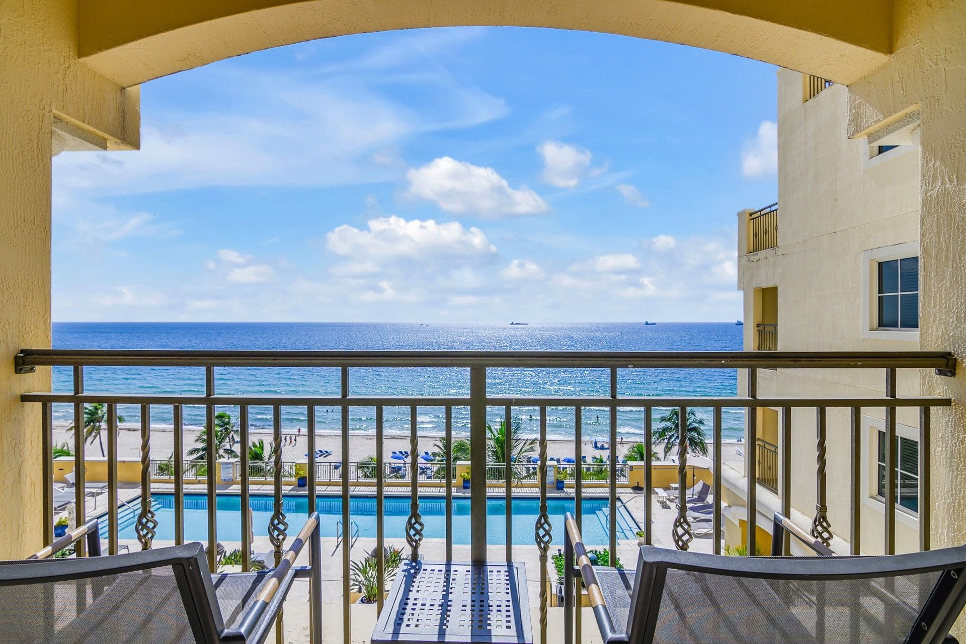 A balcony with a view of the ocean, pool, and beach