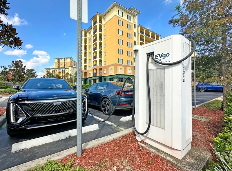 An electric vehicle charging station with two cars parked nearby in a parking lot.