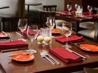 Close-up of a dining table set with wine glasses, red cloth napkins, cutlery, and small side plates at Margaux Restaurant