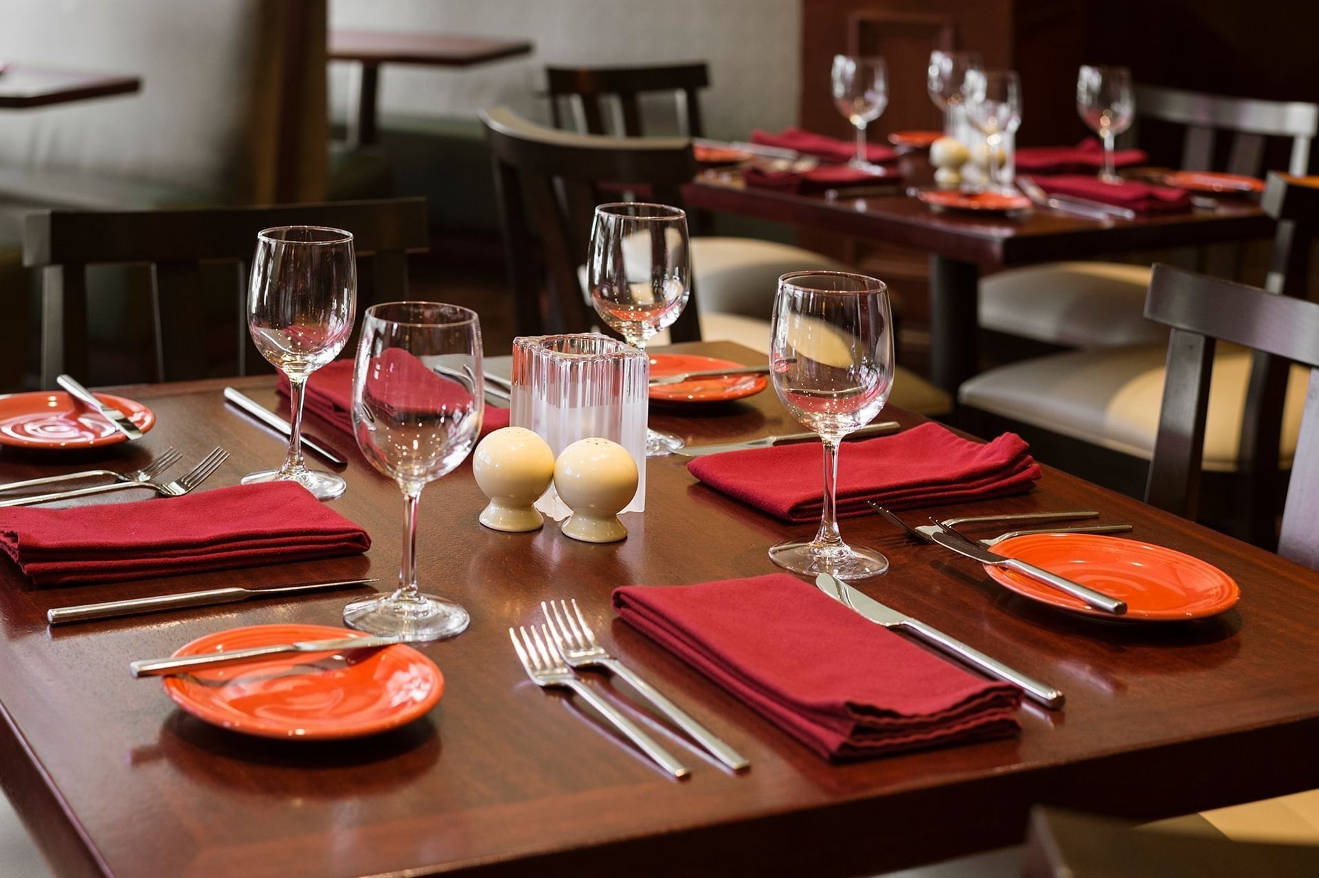 Close-up of a dining table set with wine glasses, red cloth napkins, cutlery, and small side plates at Margaux Restaurant
