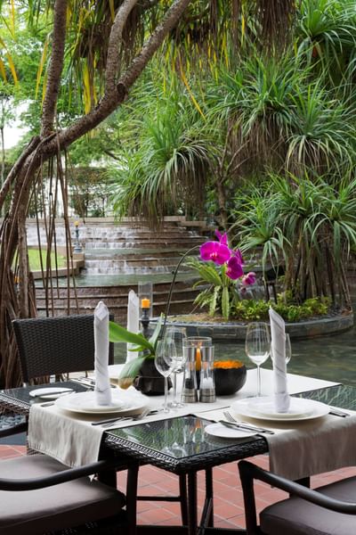 Senja dining setup with white linens, flowers, and glassware by a calm water feature at The Saujana Hotel Kuala Lumpur