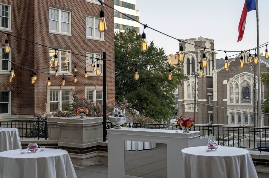 White bar by cocktail tables under hanging lights on a rooftop terrace in The Bridewell Suite at Warwick Melrose Dallas
