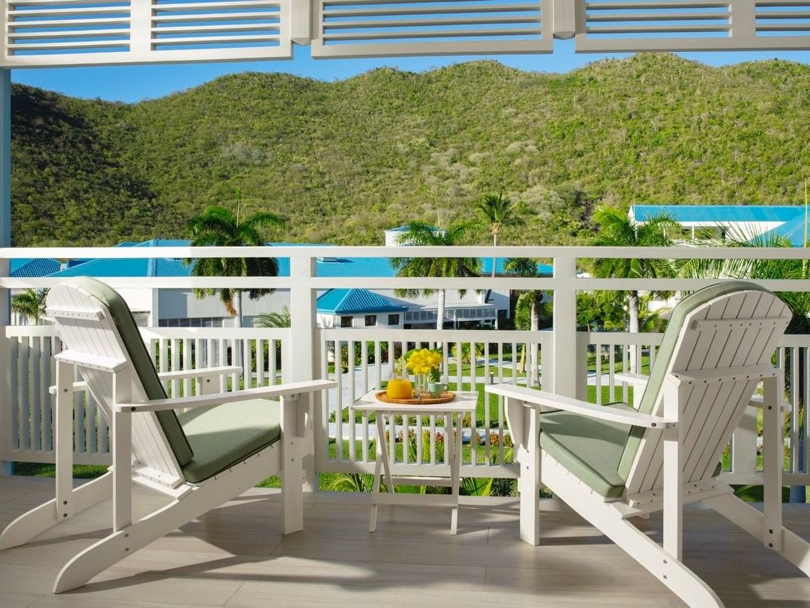 Balcony of King Bed with Courtyard View at Saint Martin Beach Resort & Spa with two chairs & a table, overlooking green hills
