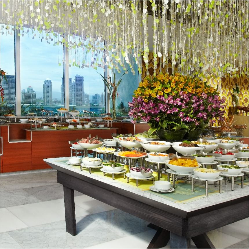 Bufé Bazaar con cuencos blancos bajo una lámpara de cuentas, junto a flores en Megapolis Hotel Panama