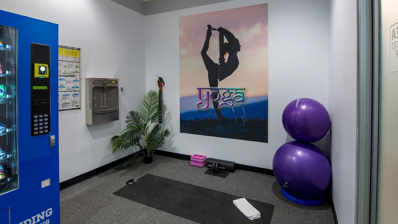 Gym with exercise balls, yoga mat, vending machine, and water dispenser.