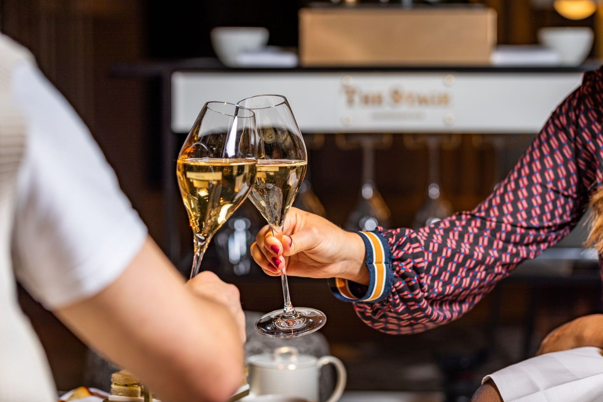 Two guests toasting with Champagne glasses in an elegant setting at The Stage, The Londoner's Hotel Champagne bar 