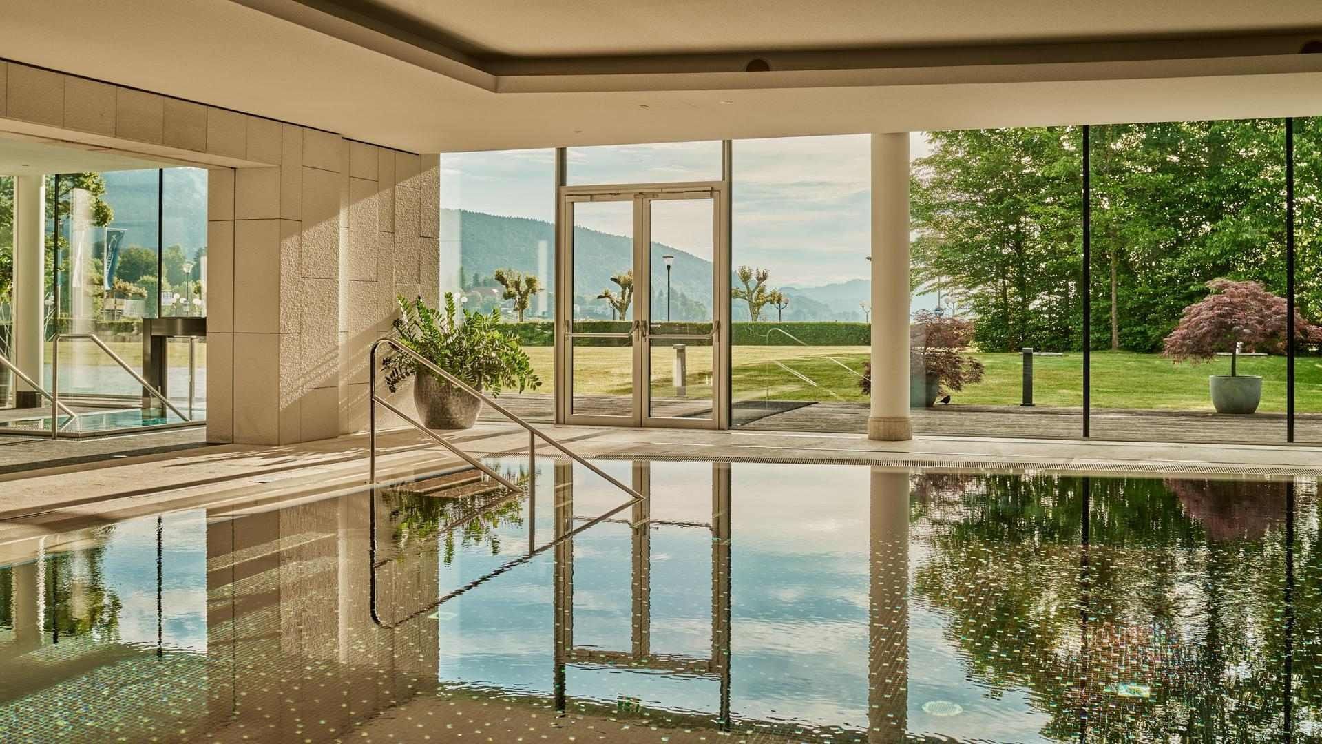 Blick auf den Innenpool mit Glaswänden und Ausblick auf Rasen und Berge.