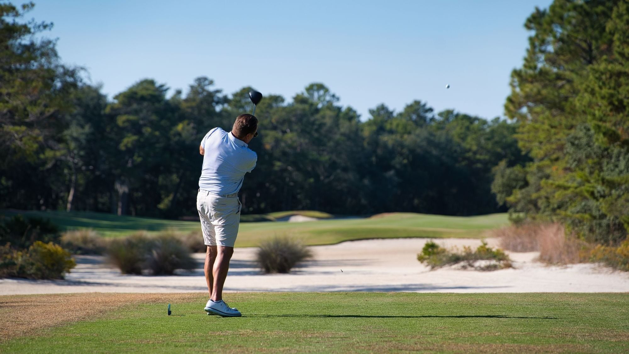 Golfer swinging club on fairway with sand bunkers during a Watersound® Golf Getaway.