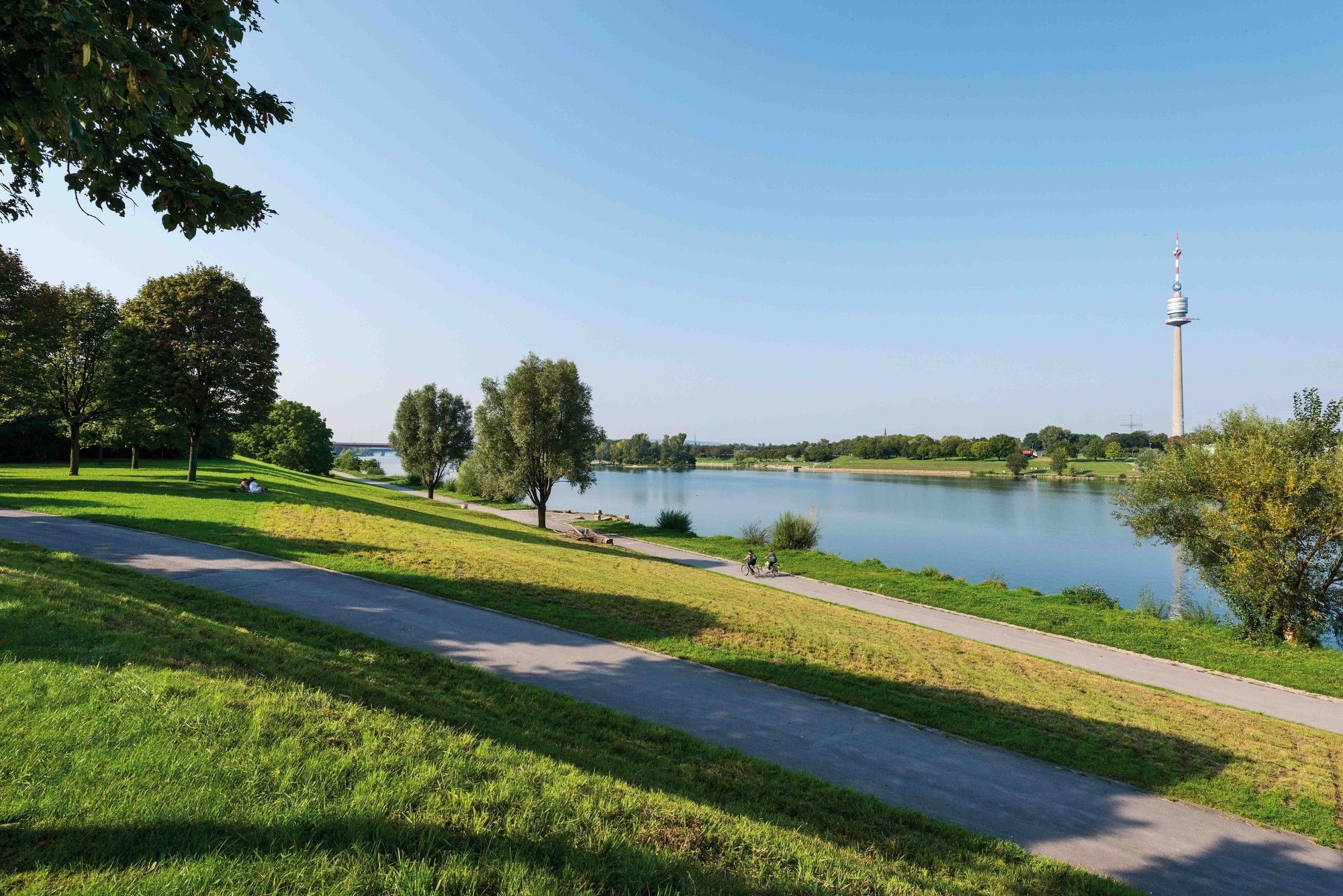 Expansive riverside scenery on the Danube Island with walking paths, green lawns, and a view of the New Danube and the Danube Tower in the background
