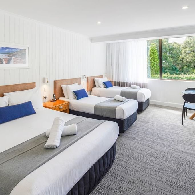 Three beds, two with blue pillows, towels, and carpeted floor at Mercure Charlestown.