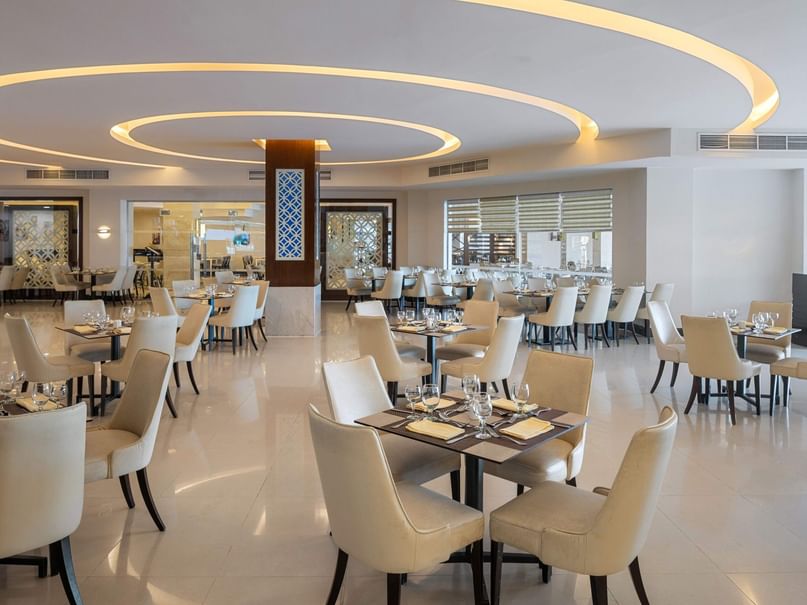 An elegant dining room with white chairs, rectangular tables, and circular ceiling lights.