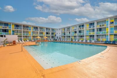 Outdoor pool area surrounded by colorful hotel balconies, umbrellas & lounge chairs at Kokomo Suites