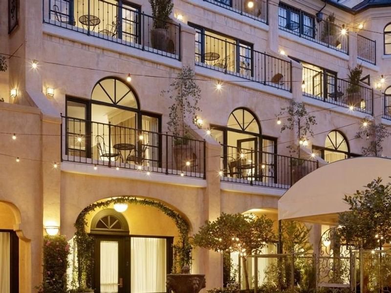 The charming exterior of El Prado Hotel at dusk, adorned with inviting string lights on balconies