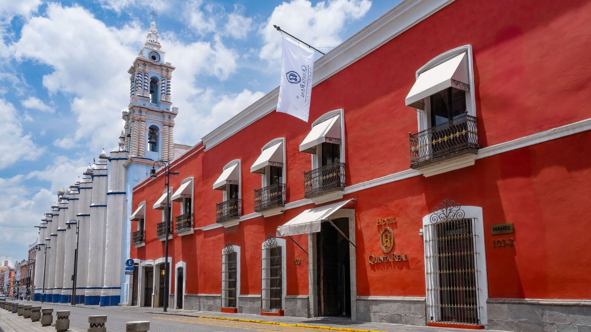 Fachada roja colonial del hotel Quinta Real junto a torre de iglesia histórica en Puebla elegante