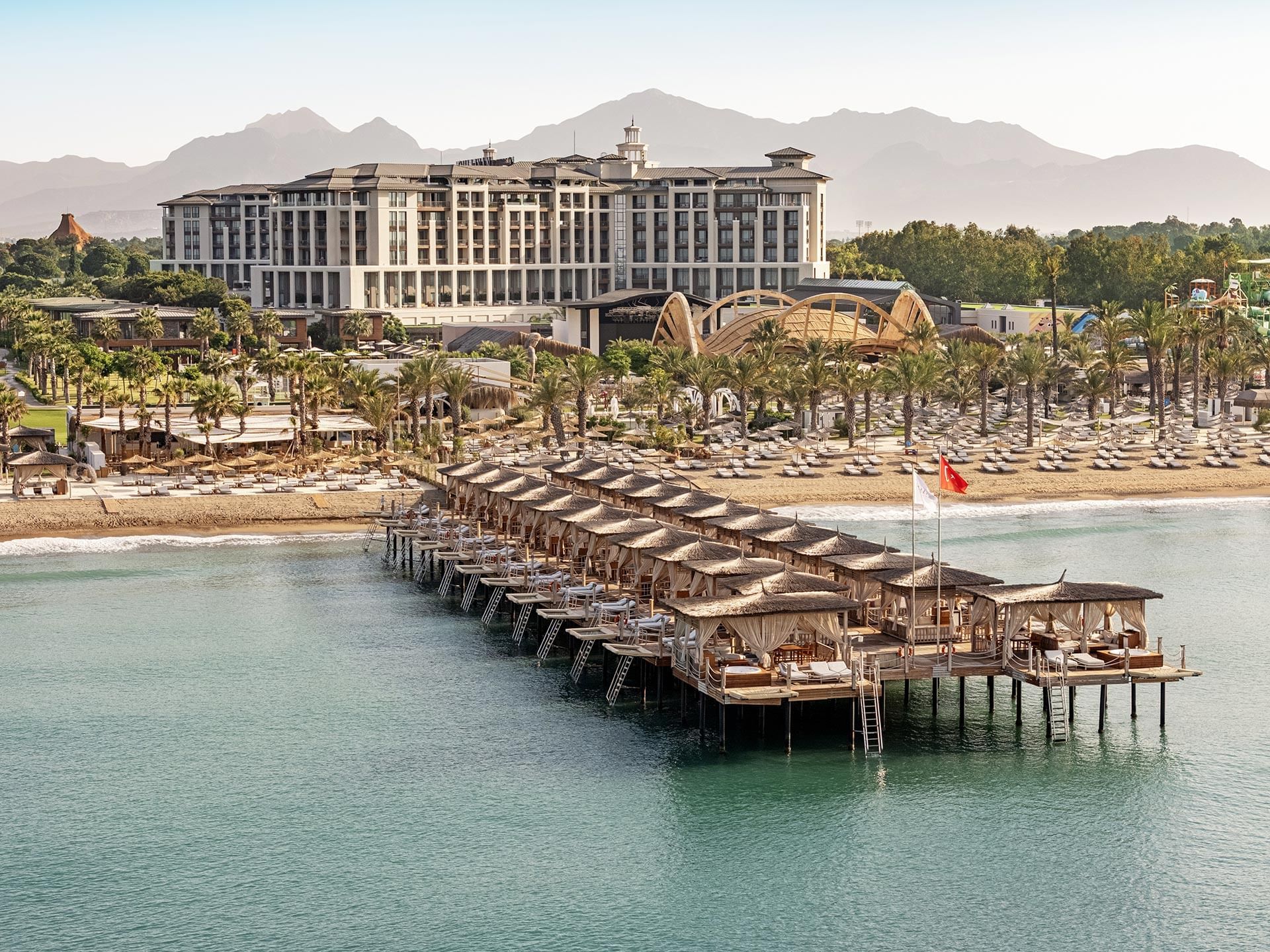 Aerial view of a resort with a pier, beach, buildings, mountains, and palm trees Cullinan Belek.